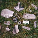 Assorted smaller aluminium wreckage including a door knob. There is also a square plate of 13.2cm side with attached square post 4cm long. The base plate retains a single rusty iron screw 6cm long. Scale in cm and inches.